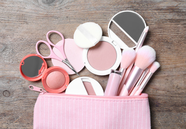 Photo of Cosmetic bag with makeup products and beauty accessories on wooden background, flat lay