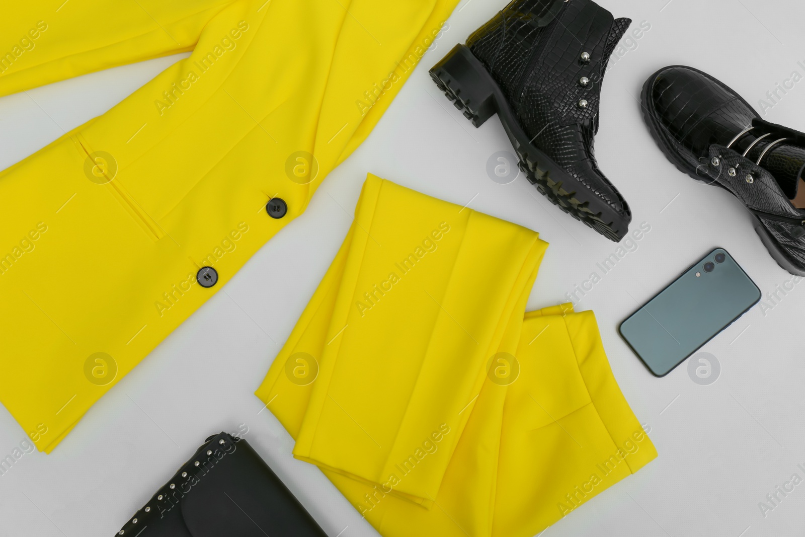 Photo of Stylish ankle boots, smartphone and yellow office suit with bag on white background, top view