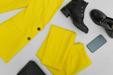 Photo of Stylish ankle boots, smartphone and yellow office suit with bag on white background, top view