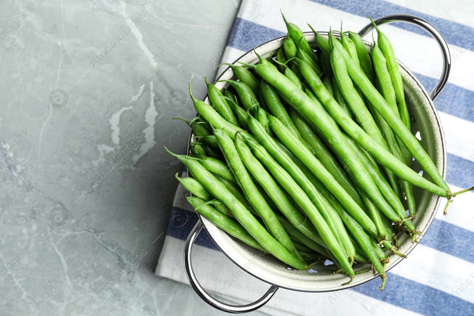 Photo of Fresh green beans in colander on grey marble table, top view. Space for text