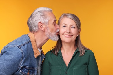 Photo of Senior man kissing his beloved woman on orange background