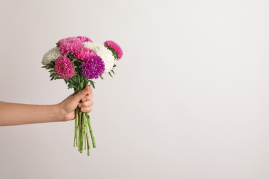 Photo of Woman holding beautiful aster flower bouquet against light background. Space for text