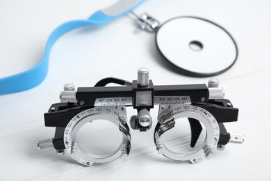 Photo of Trial frame and head mirror on white wooden table, closeup