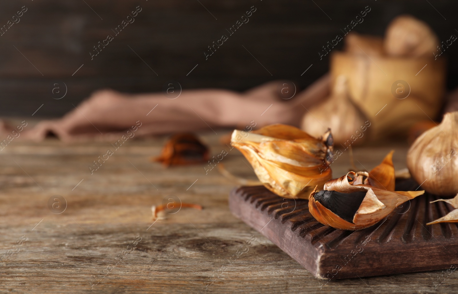 Photo of Board with black garlic on wooden table. Space for text