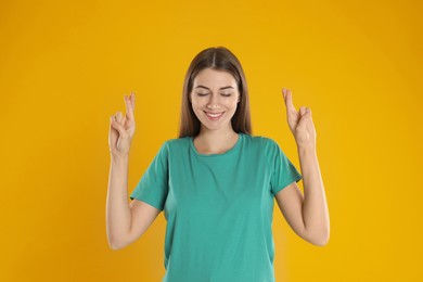 Photo of Woman with crossed fingers on yellow background. Superstition concept