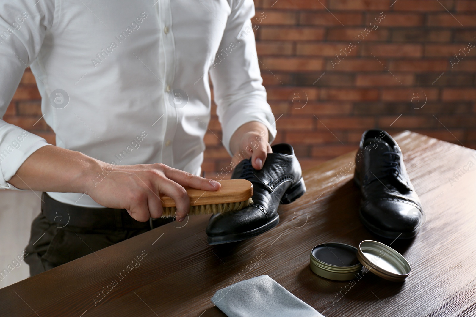 Photo of Man cleaning leather shoe at wooden table indoors, closeup