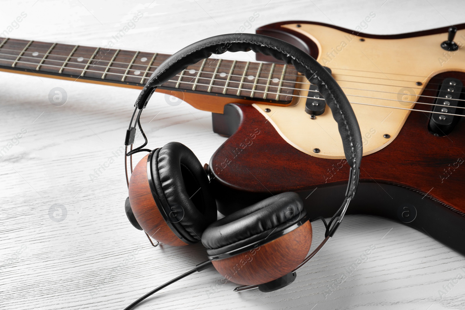 Photo of Modern electric guitar with headphones on wooden background. Musical instrument