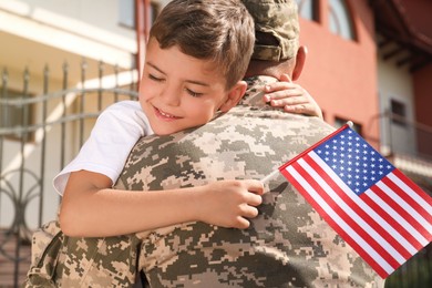 Soldier and his little son with flag of USA hugging outdoors