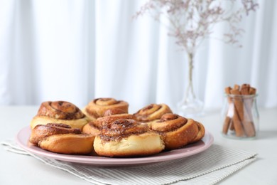 Many tasty cinnamon rolls on white table, space for text