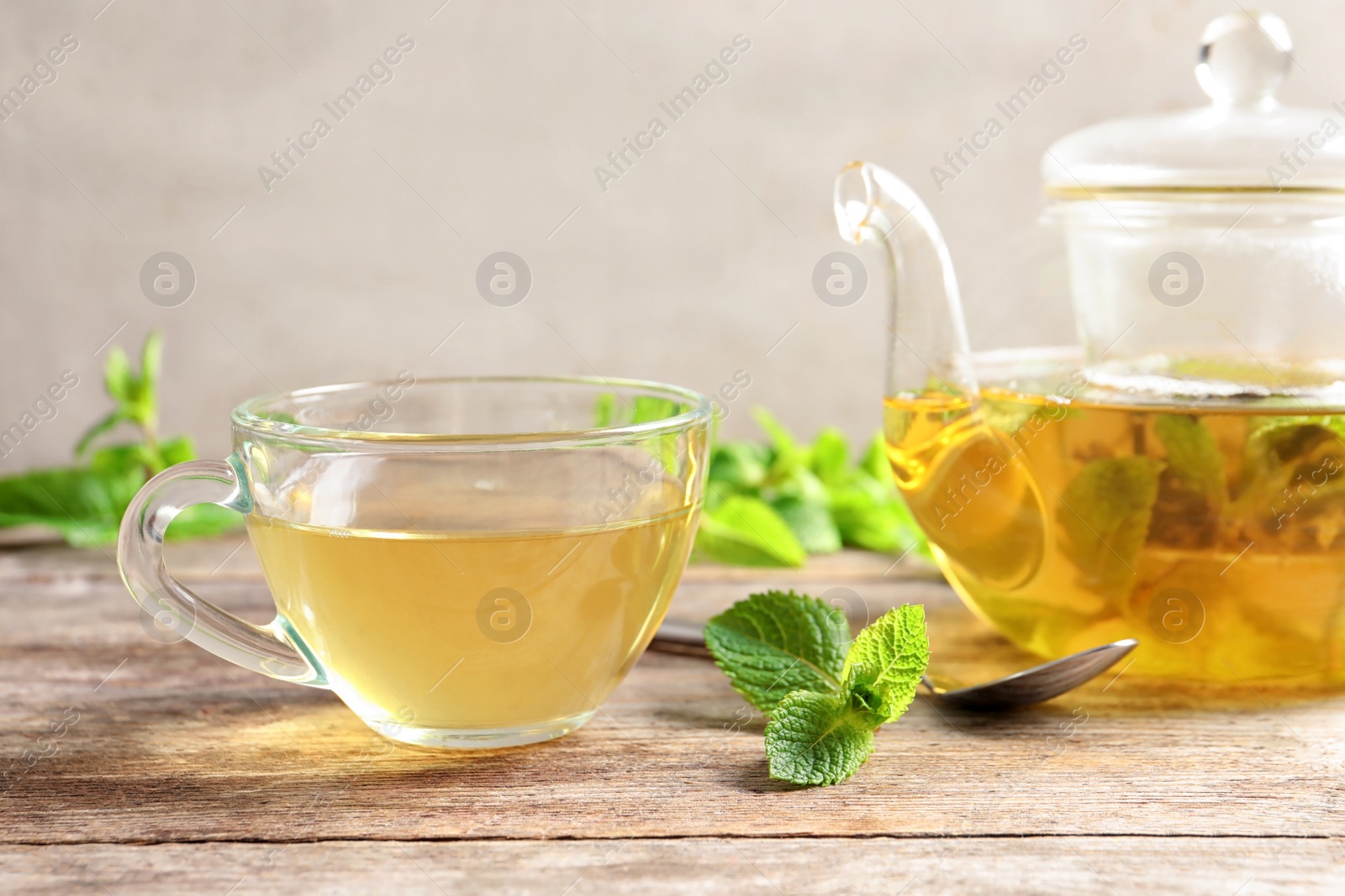 Photo of Cup and teapot with hot aromatic mint tea on wooden table