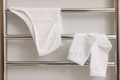 Photo of Heated towel rail with underwear and socks on white wall, closeup