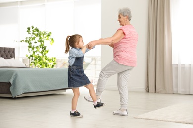 Photo of Cute girl and her grandmother dancing at home