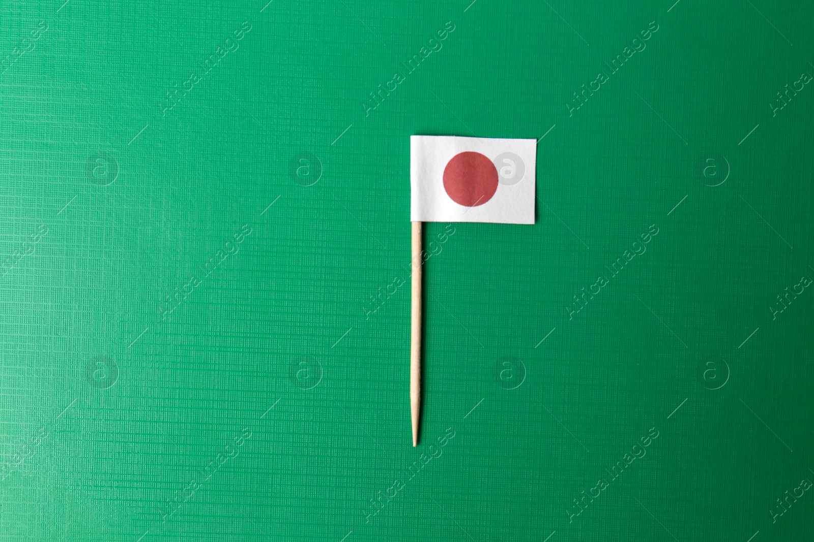 Photo of Small paper flag of Japan on green background, top view. Space for text