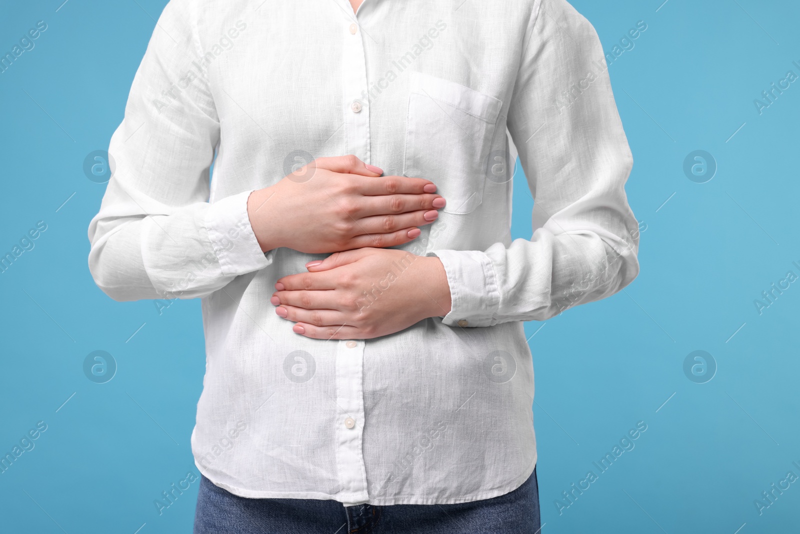 Photo of Young woman suffering from stomach pain on light blue background, closeup