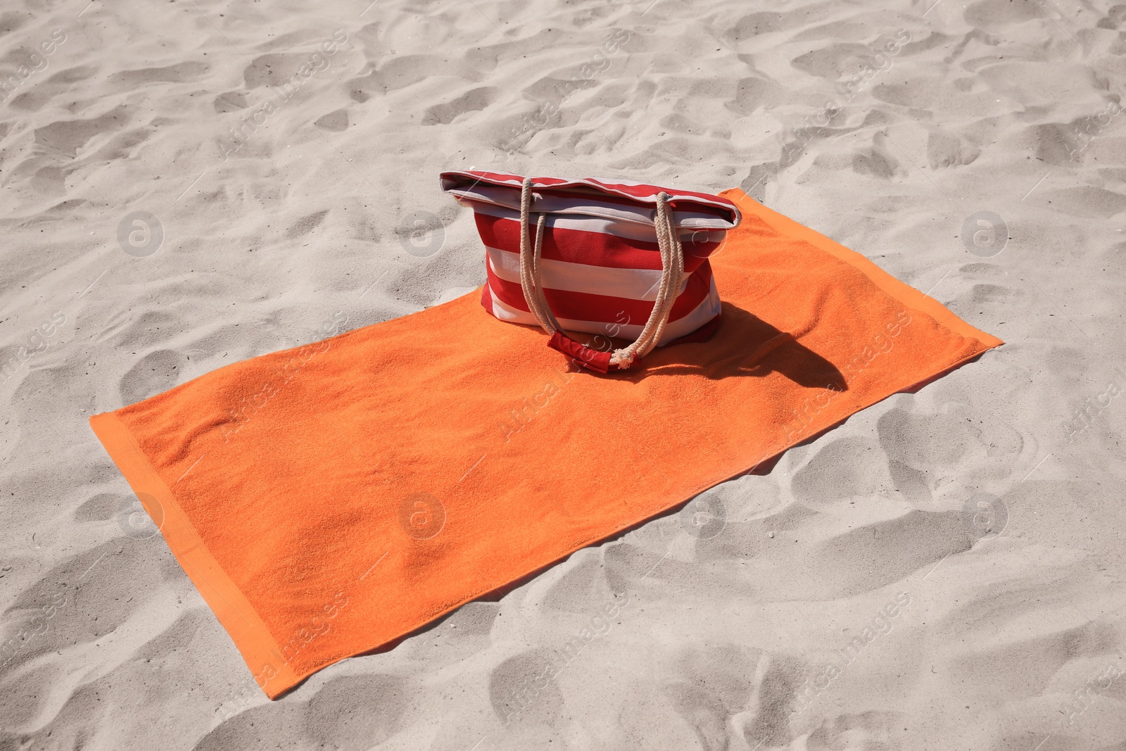 Photo of Soft orange beach towel and bag on sand