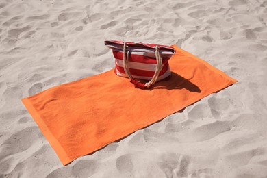 Photo of Soft orange beach towel and bag on sand