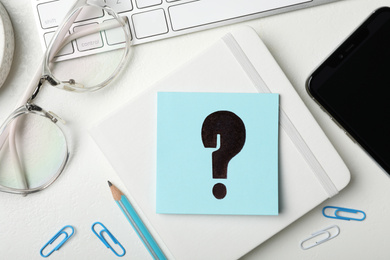 Photo of Notebook, eyeglasses and sheet of paper with question mark on white table, flat lay