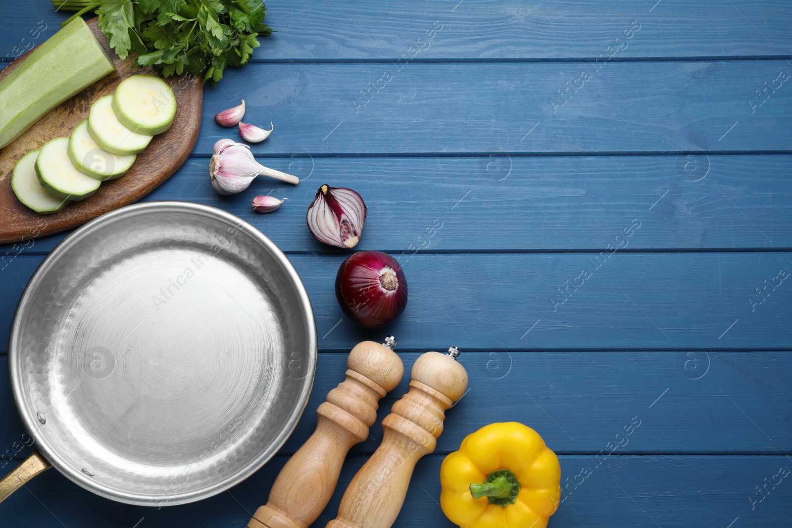 Photo of Flat lay composition with empty frying pan and fresh vegetables on blue wooden table, space for text