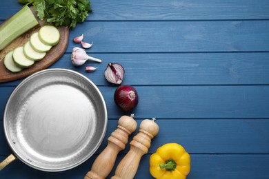 Photo of Flat lay composition with empty frying pan and fresh vegetables on blue wooden table, space for text