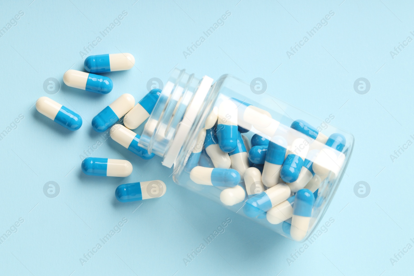 Photo of Antibiotic pills and bottle on light blue background, top view