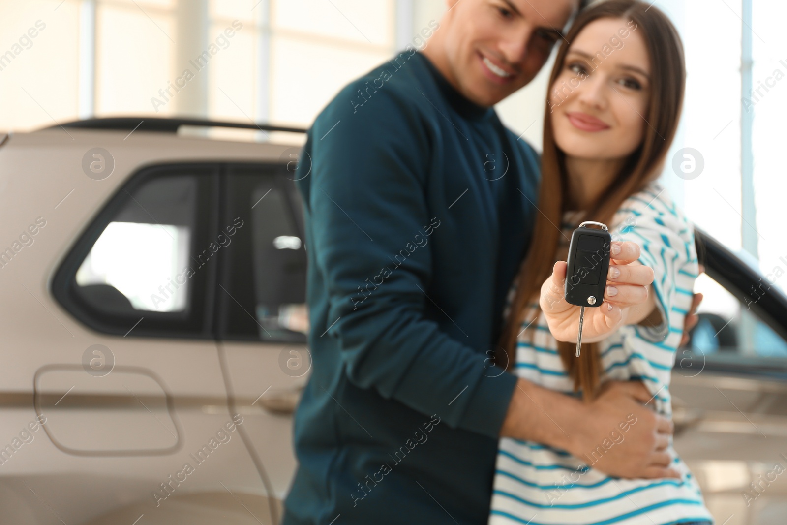 Photo of Happy couple with car key in modern auto dealership, focus on hand