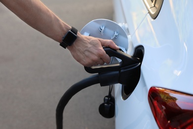 Photo of Man inserting plug into electric car socket at charging station, closeup