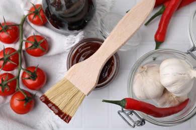 Photo of Marinade in jar, ingredients and basting brush on white tiled table, flat lay