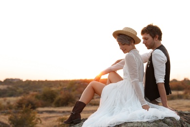 Happy newlyweds sitting on rock at sunset