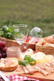 Picnic blanket with wineglasses and food on green grass