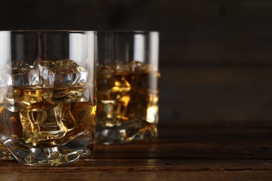 Photo of Whiskey with ice cubes in glasses on wooden table, closeup. Space for text