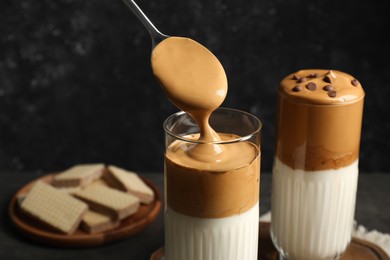 Photo of Pouring cream for dalgona coffee into glass on dark table, closeup