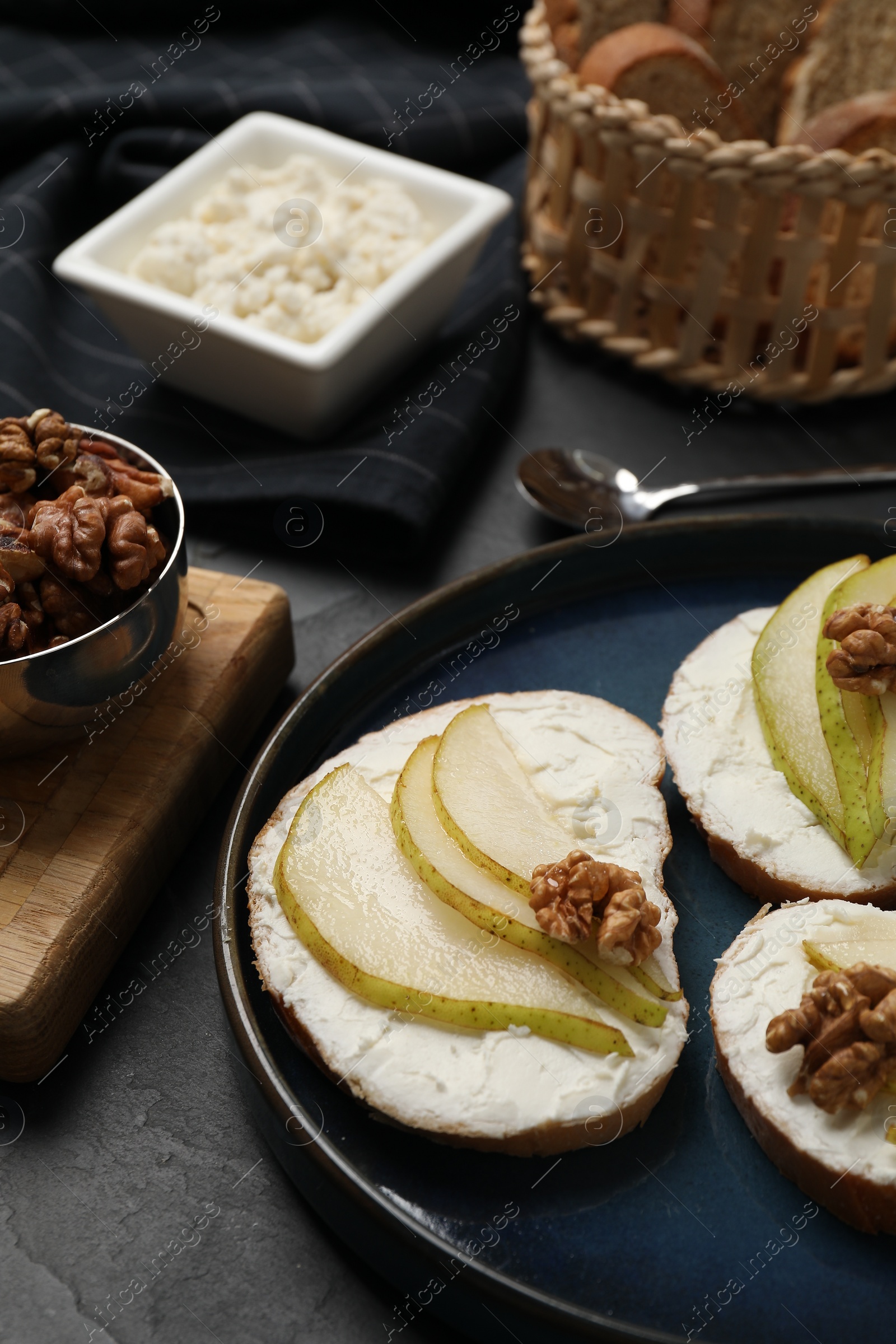 Photo of Delicious bruschettas with ricotta cheese, pears and walnuts on dark table, closeup