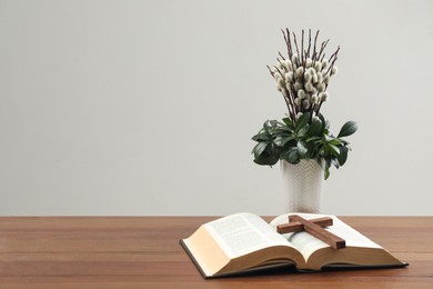 Bible, plant with willow branches and cross on wooden table, space for text