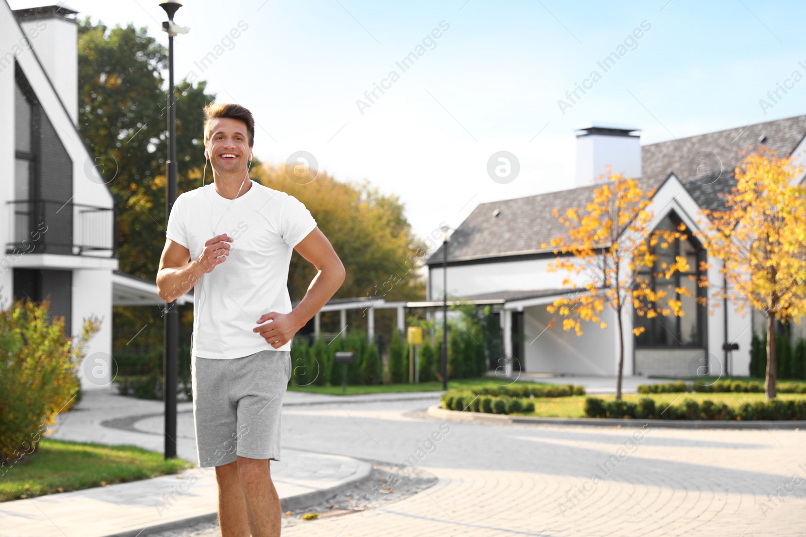 Photo of Young man with earphones running outdoors on sunny morning. Healthy lifestyle