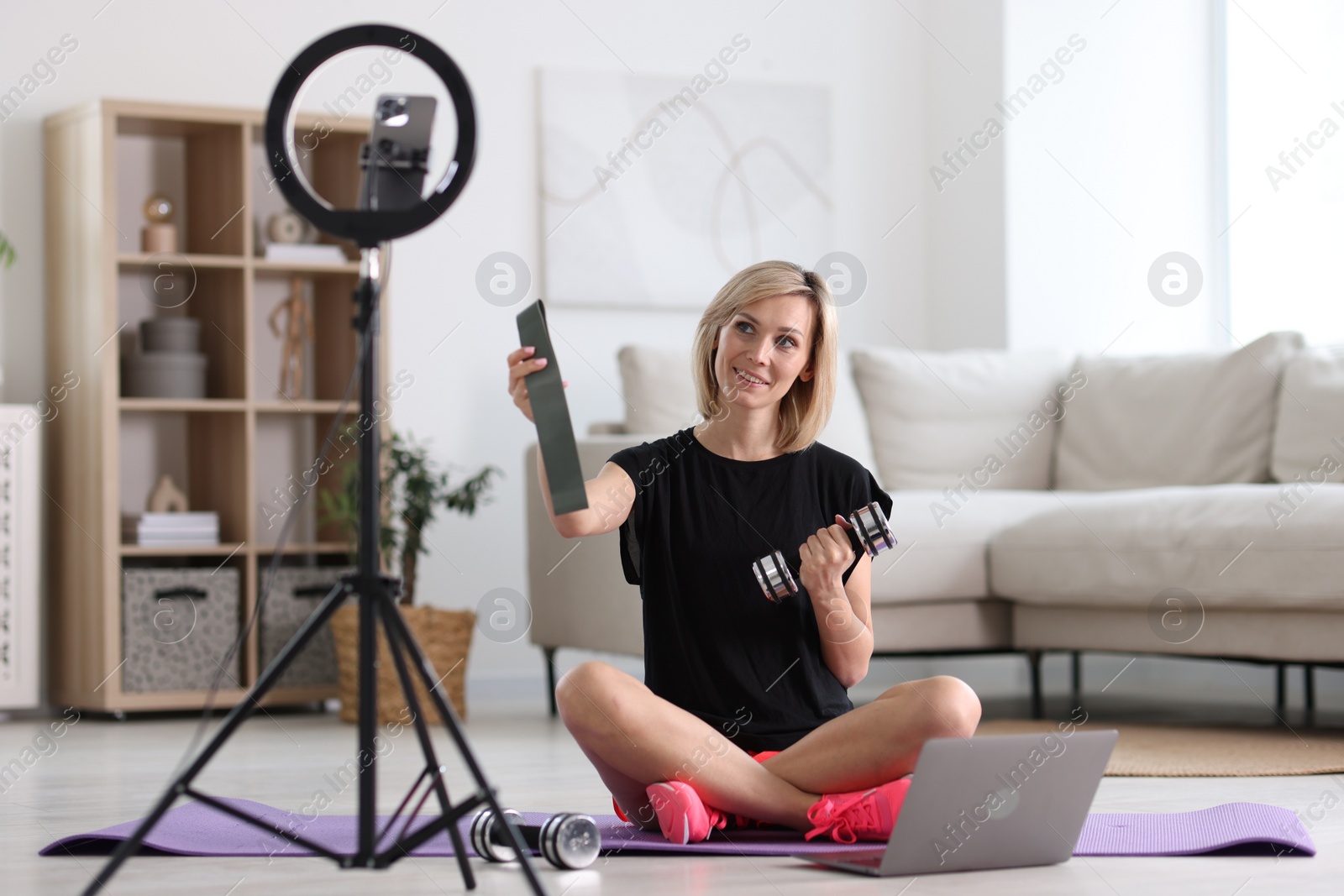 Photo of Smiling sports blogger streaming online fitness lesson with smartphone at home