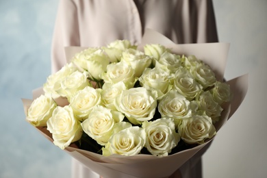 Photo of Woman holding luxury bouquet of fresh roses on light blue background, closeup