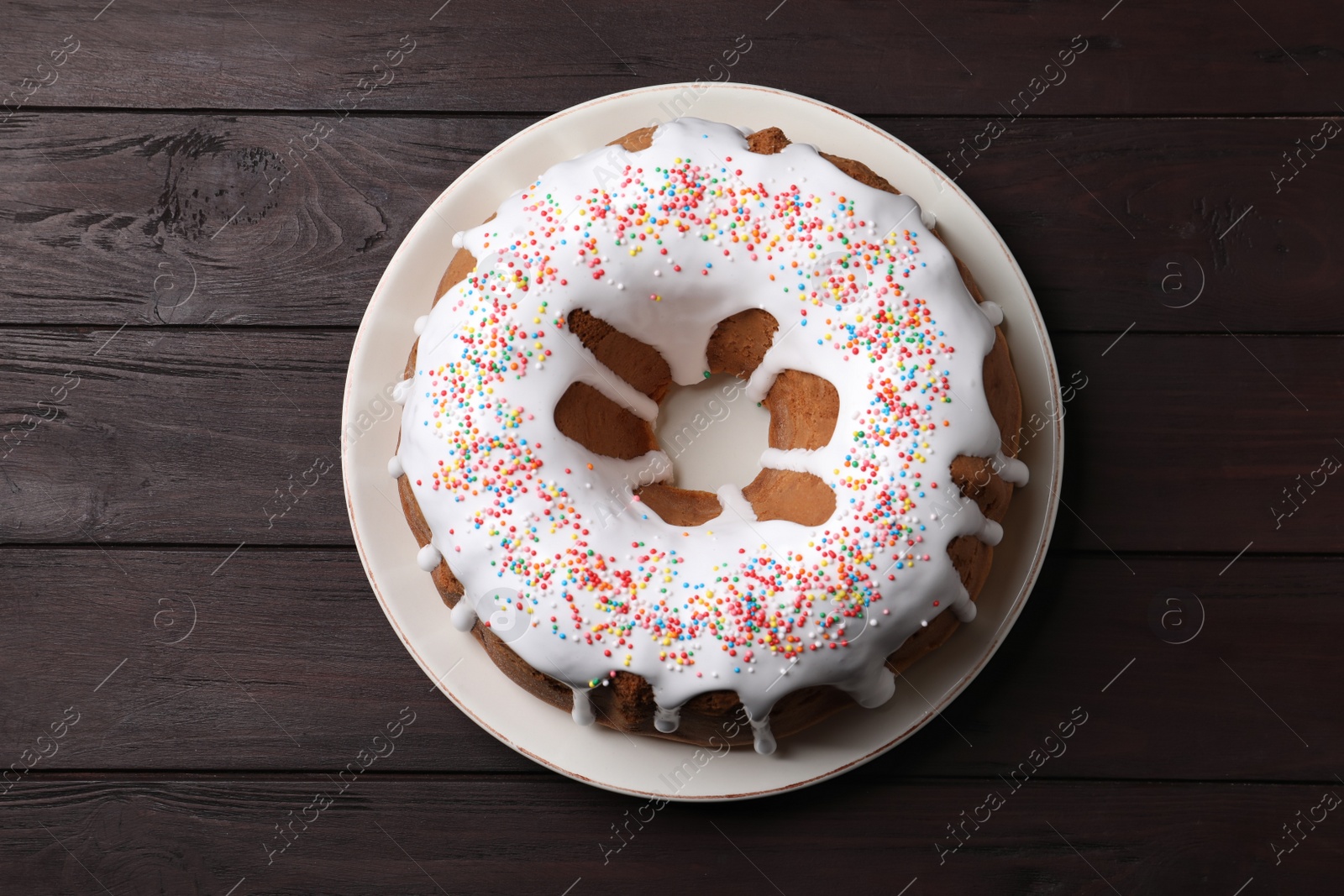 Photo of Glazed Easter cake with sprinkles on wooden table, top view