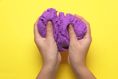 Woman playing with kinetic sand on yellow background, top view