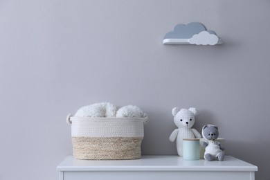 Photo of Child's toys, wicker basket and accessories on chest of drawers near light grey wall indoors
