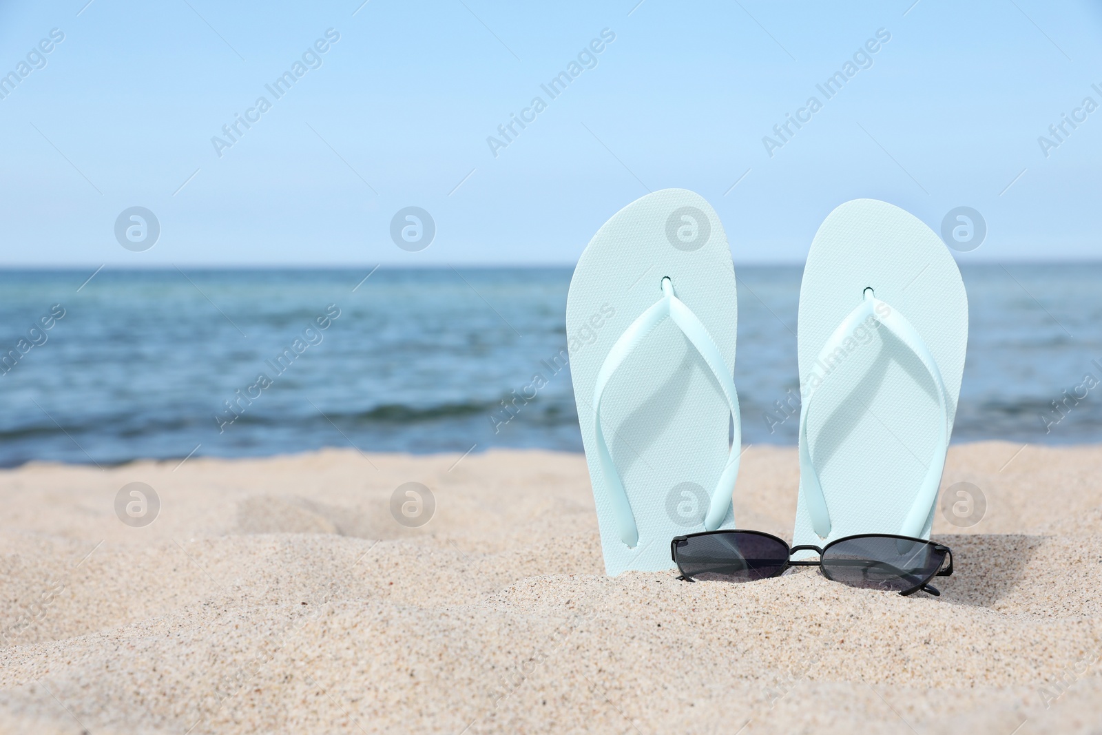 Photo of Stylish light blue flip flops and sunglasses on beach sand, space for text