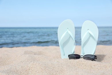 Photo of Stylish light blue flip flops and sunglasses on beach sand, space for text