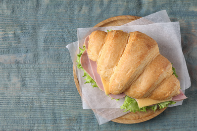 Photo of Tasty croissant sandwich with ham on light blue wooden table, top view