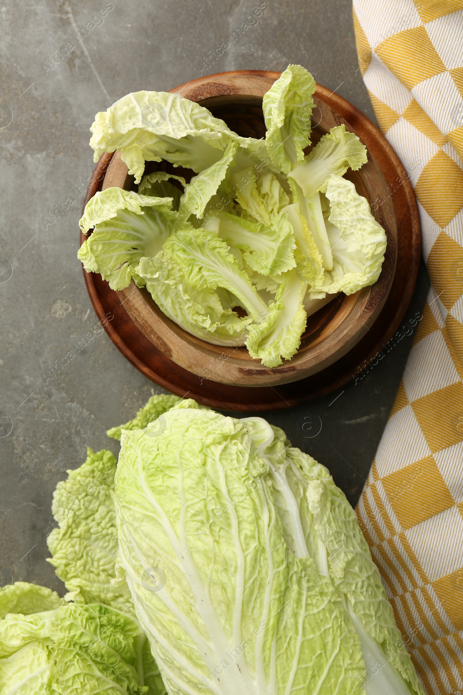 Photo of Fresh ripe Chinese cabbages and green leaves in bowl on gray table, flat lay