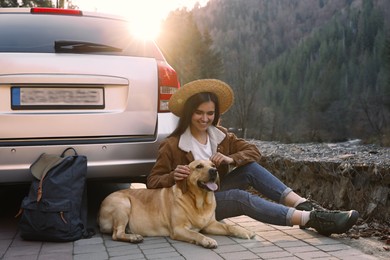 Photo of Happy woman and adorable dog sitting near car in mountains. Traveling with pet