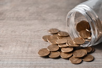 Photo of Glass jar with coins on wooden table, closeup. Space for text