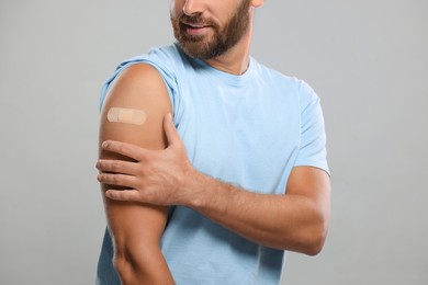 Photo of Man with sticking plaster on arm after vaccination against light grey background, closeup