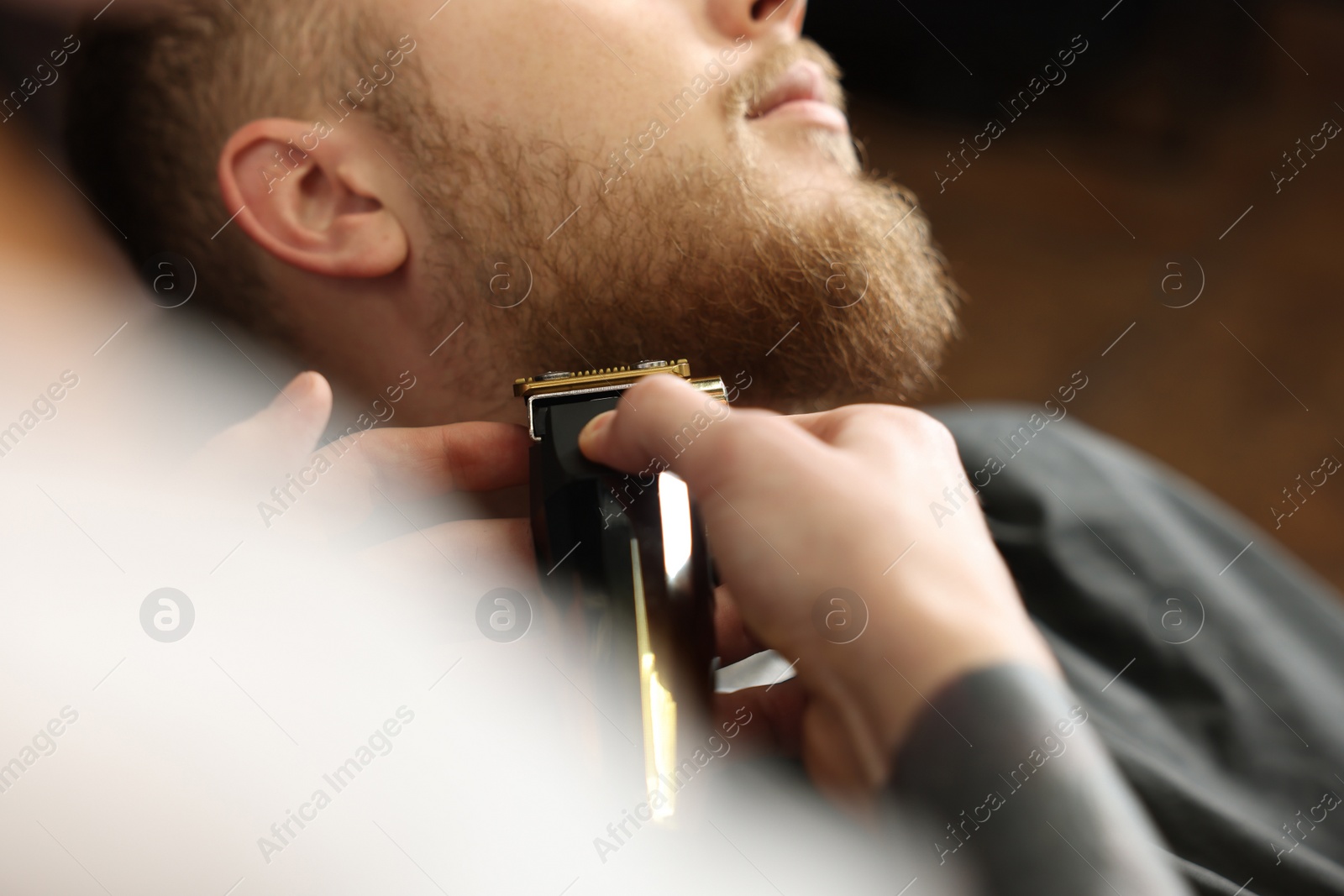 Photo of Professional hairdresser working with bearded client in barbershop, closeup