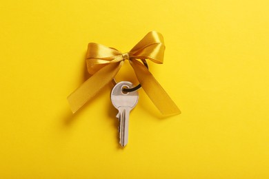 Photo of Key with color bow on yellow background, top view. Housewarming party