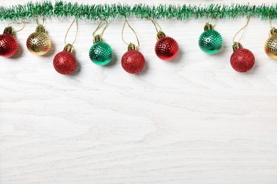 Bright tinsel and Christmas balls on white wooden background, flat lay. Space for text