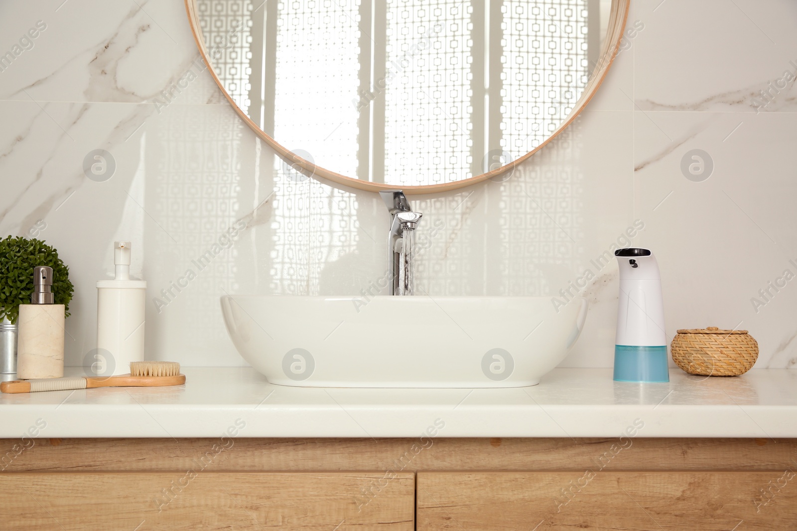 Photo of Modern automatic soap dispenser and other toiletries on countertop in bathroom